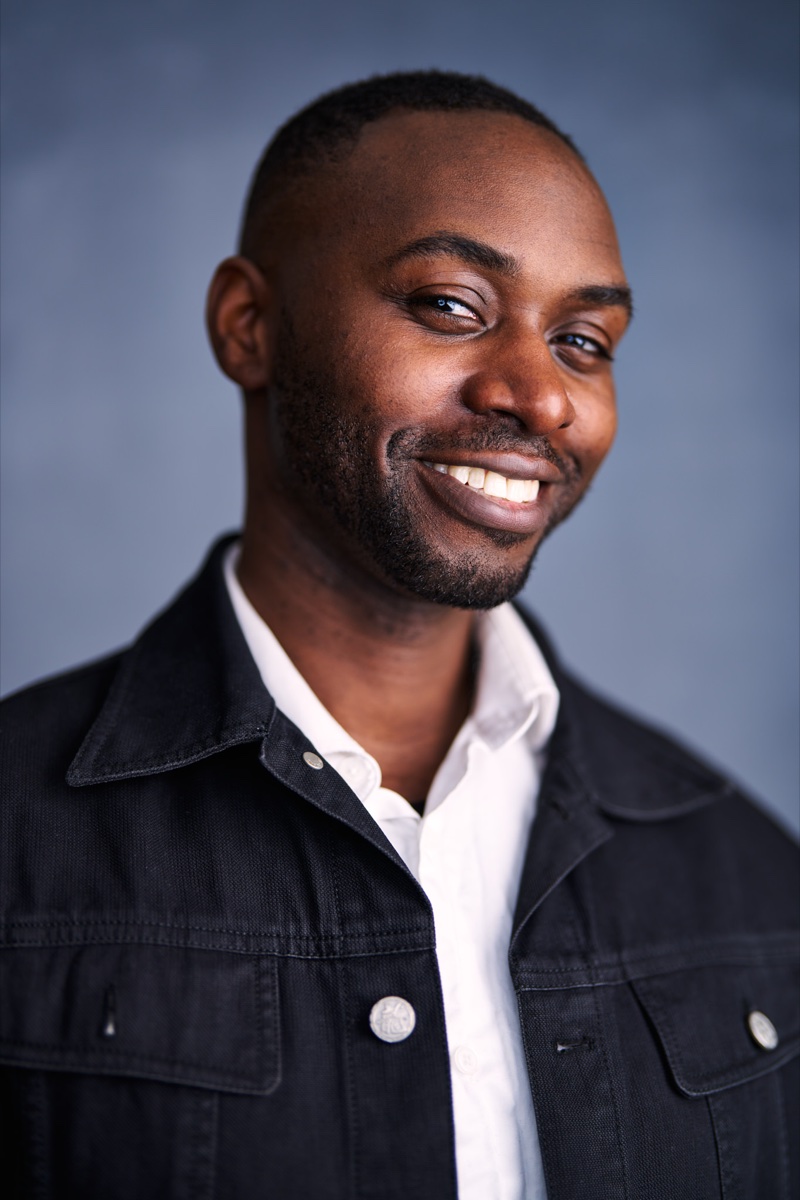 Richard smiling in a dark jacket and white shirt against a blue-grey background